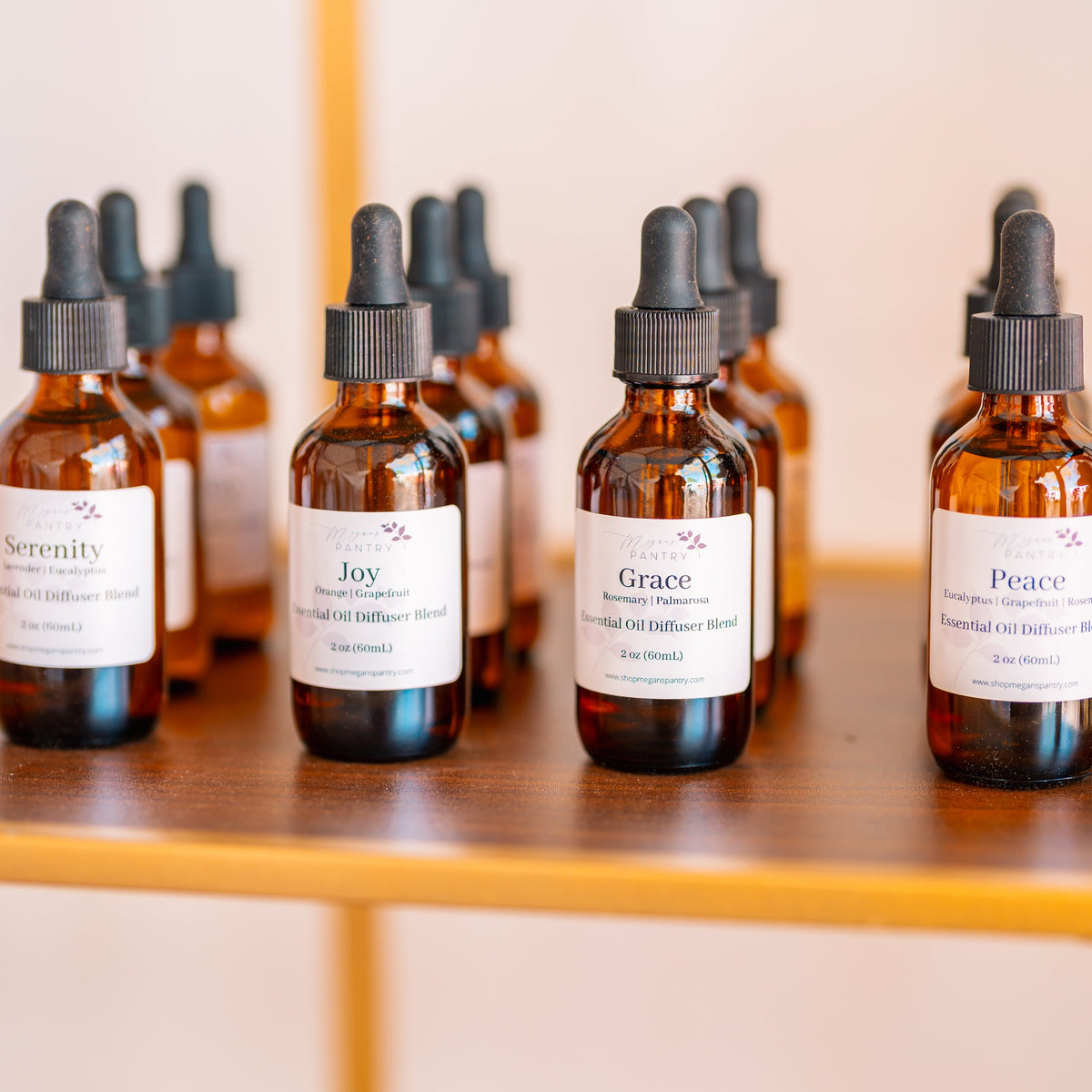 Four amber bottles of Serenity, Joy, Grace and Peace essential oil blends lined up beside a wooden diffuser