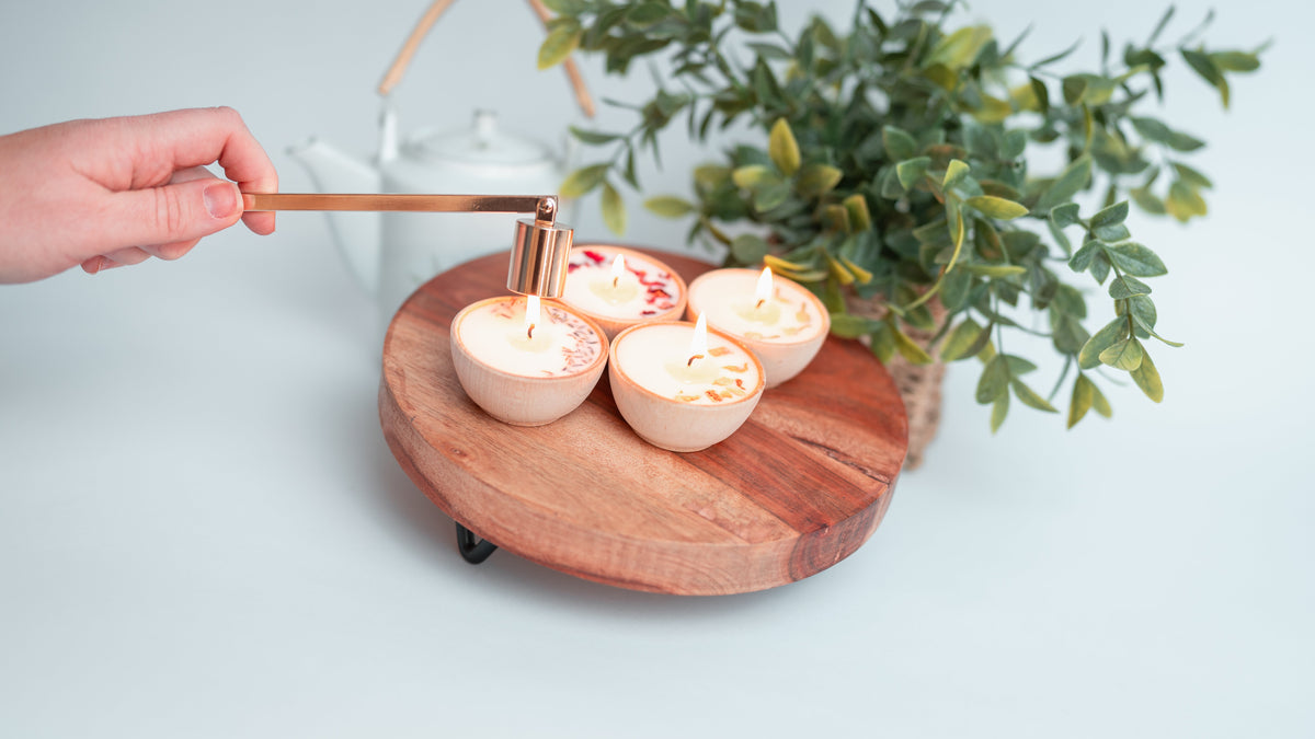 Hand-poured essential oil soy candle glowing on a wooden table beside wooden safety matches and a gold candle snuffer