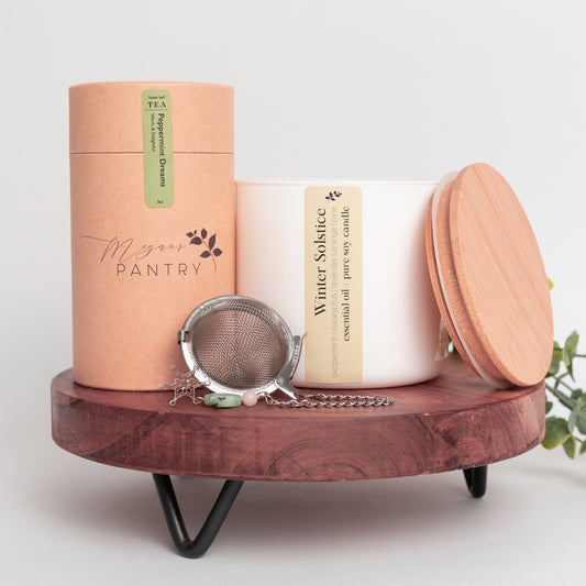 Megan’s Pantry 2025 Holiday Gift Set featuring a winter wellness tea gift box with Peppermint Dreams herbal loose leaf tea (3 oz), a hand-poured soy Winter Solstice Candle (16 oz) with pure essential oils, and a stainless steel snowflake tea ball infuser ornament displayed in a cozy, seasonal setting perfect for Christmas gifting, tea lovers, and holiday self-care.