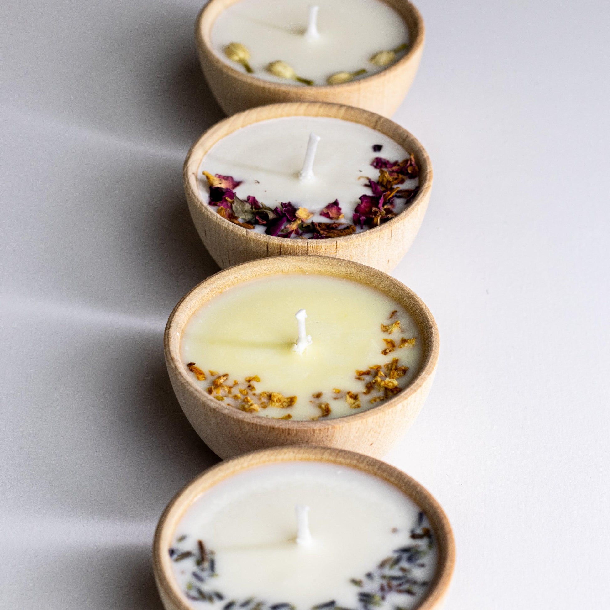 Set of four essential oil soy tealight candles from Megan’s Pantry in reusable wooden bowls, adorned with botanicals—natural, eco-friendly aromatherapy gift set.