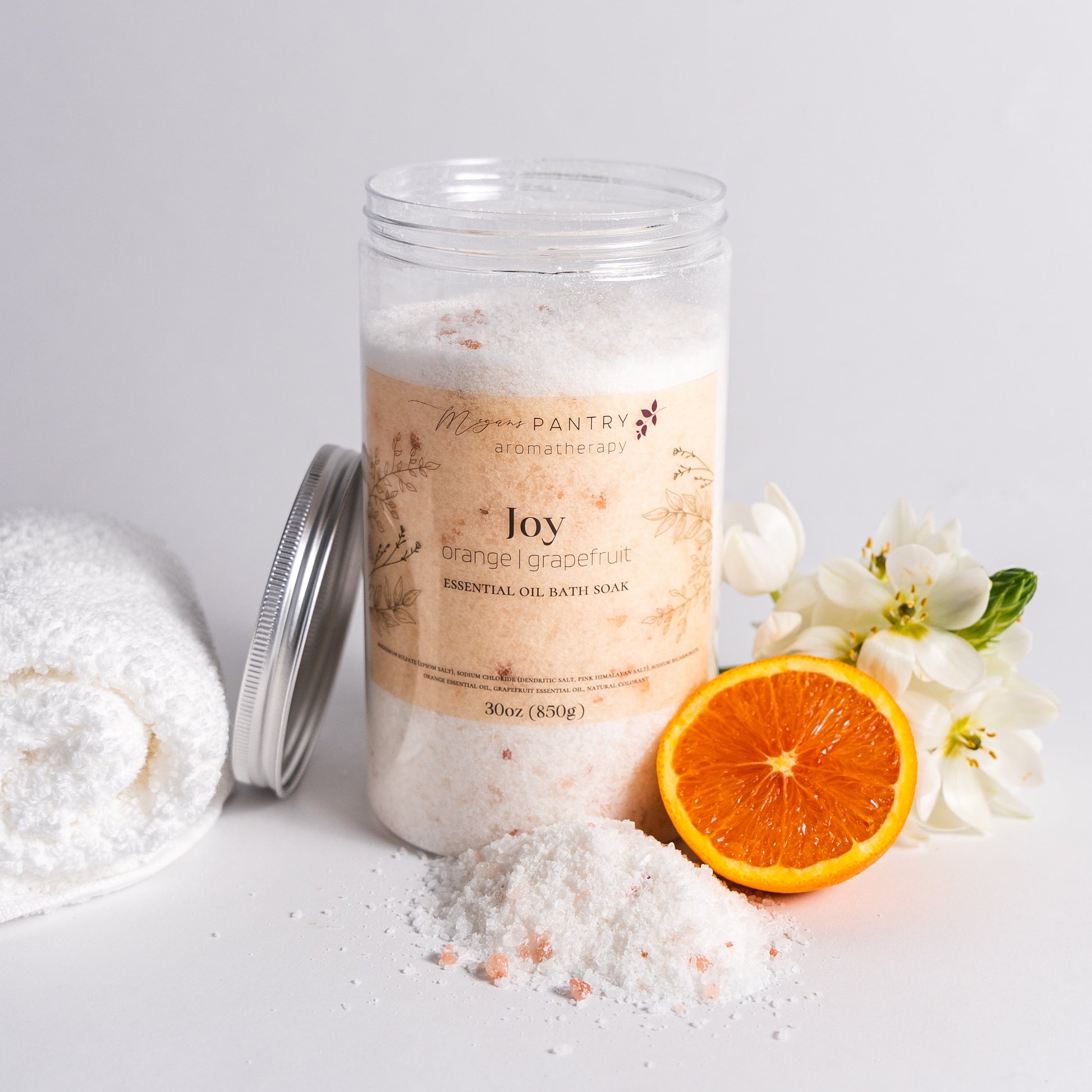 Jar of bath salts with a towel, orange, and flowers on a light gray background